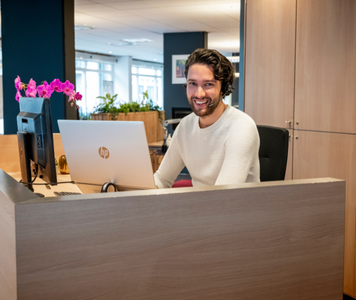Intercedent met headset lacht achter laptop.