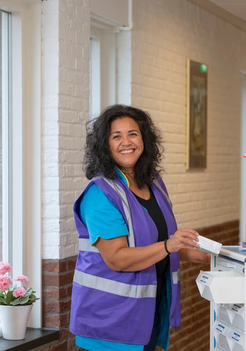 Zorgmedewerker staat bij een verrijdbare werkwagen in de gang van een zorglocatie.