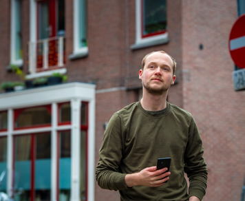 Kandidaat met telefoon in zijn hand loopt door een straat met woningen op de achtergrond.