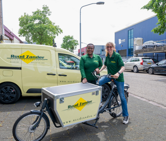 Twee kandidaten staan met een bakfiets voor een bedrijfsbus.