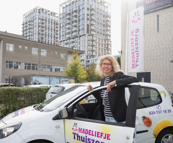 Verpleegkundige van Madeliefje Thuiszorg stapt lachend uit een dienstauto voor een zorgbezoek.
