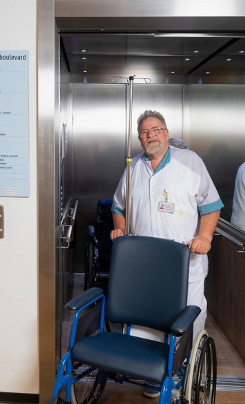 Zorgmedewerker verplaatst een rolstoel vanuit een lift in een zorginstelling.