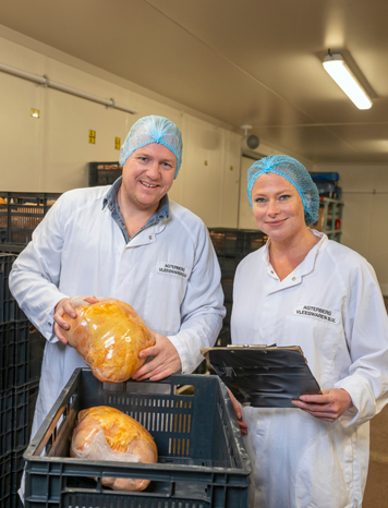 Twee productiemedewerkers in witte jassen en blauwe haarnetjes controleren verpakte voedingsproducten in een krat in een gekoelde productieruimte.