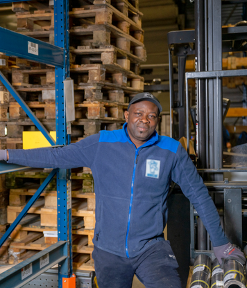 Magazijnmedewerker leunt tegen stelling en reachtruck in het magazijn.