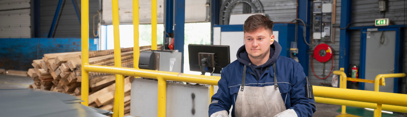 Man in blauwe werkkleding werkt geconcentreerd in een fabriekshal met machines.