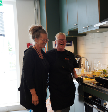 Woonbegeleider lacht samen met collega in de keuken tijdens een huiselijke activiteit
