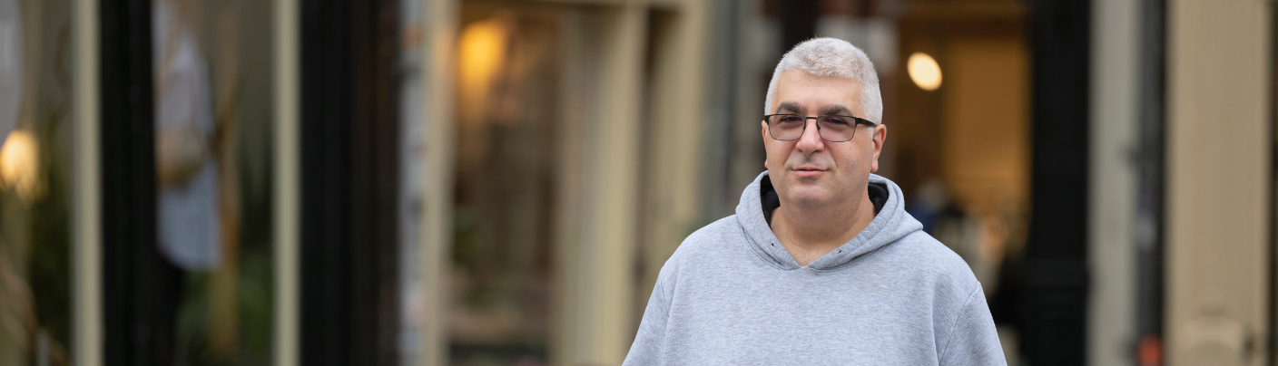 Kandidaat in grijze hoodie poseert in een historische winkelstraat.