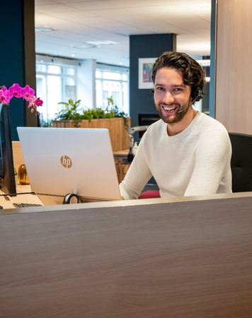 Intercedent met headset lacht achter laptop.